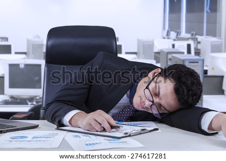 Young businessperson sleeping in the office with paperwork on the table