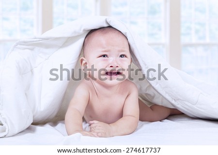 Baby boy crying under blanket at home