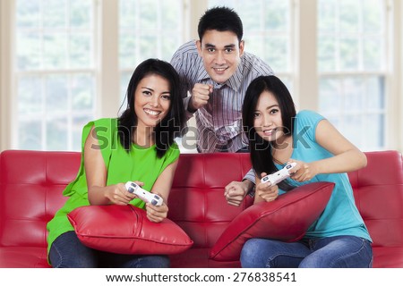 Group of asian people sitting on the sofa while playing video games with joystick at home
