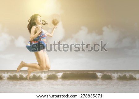 Portrait of cheerful woman wearing swimwear, jumping on the beach, shot with an instagram effect