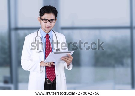 Male doctor standing near the window while using a digital tablet in the hospital