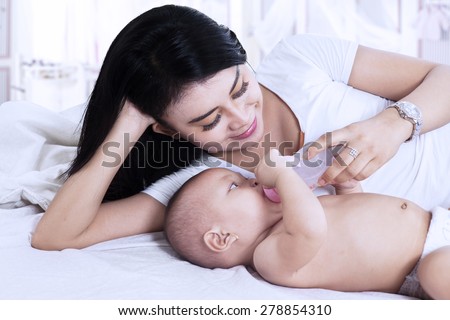 Asian mother feeding her baby with milk on the bedroom