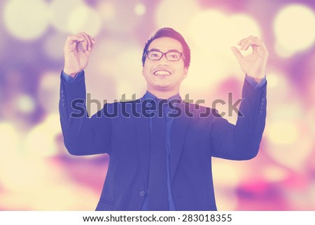 Happy male worker celebrating his winning and raised hands, shot with festive light background