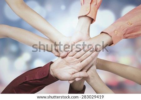 Closeup of business people joining hands together, shot against bokeh background