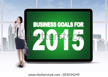 Young businesswoman standing in office near a billboard with business goals for 2015