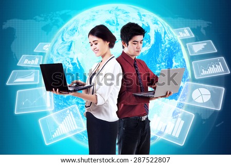 Two young entrepreneurs working with laptop in front of futuristic global business statistics