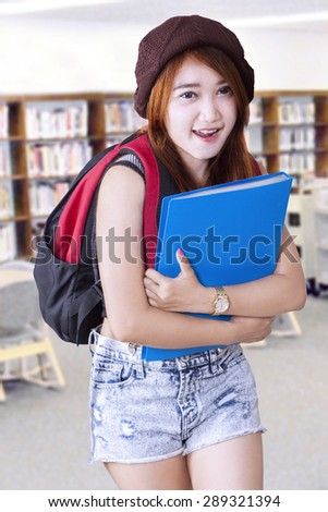 Gorgeous teenage girl carrying a backpack and folder in the library at school