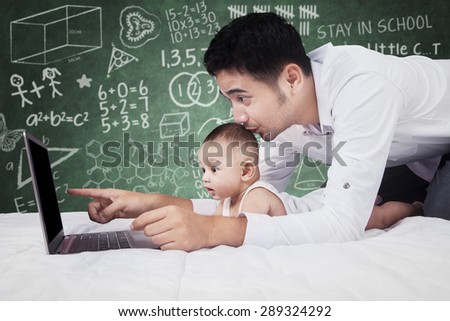 Portrait of young father teach his baby with laptop and showing something on the screen