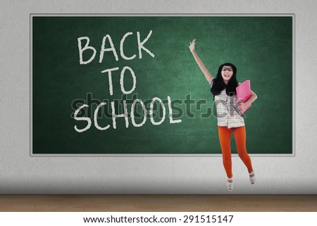 Happy student back to school jumping in front of blackboard