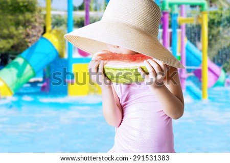 Closeup of female child wearing a big hat on the pool while eating a fresh watermelon