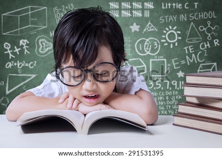 Portrait of a cute female student using glasses to read textbooks in the classroom
