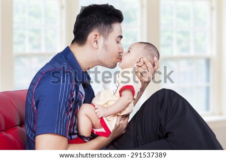 Young father holding his baby on sofa and kiss the baby's lips, shot at home