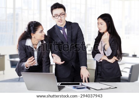 Three businesspeople working together in a meeting with laptop and debating in the office