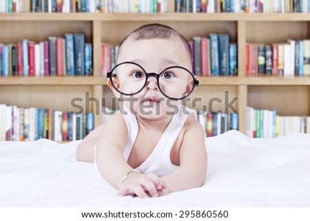 Lovely male infant wearing glasses and looking at the camera, shot with a bookshelf background
