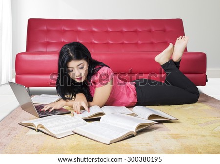 Portrait of female high school student studying with laptop and books while lying on the carpet at home near the sofa