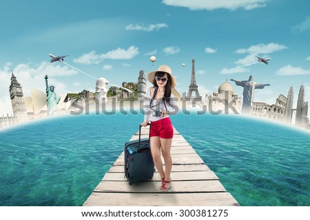 Trendy young woman travelling to the worldwide monument by carrying luggage and digital camera