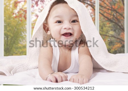 Portrait of a cute little baby boy laughing on the bed under a towel and look at the camera