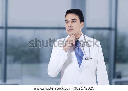 Portrait of young handsome doctor thinking about something with hand on chin