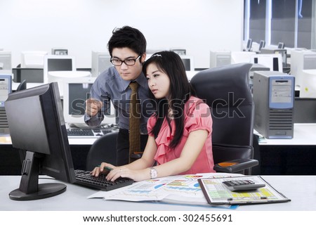Young businessman help his partner by showing the task on the monitor, shot in the office