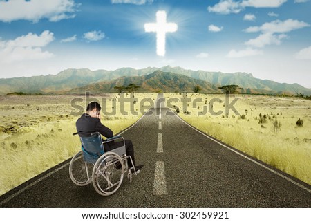 Businessman sitting in the wheelchair on the road with a cross on the sky