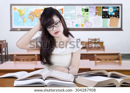 Portrait of high school student with long hair studying in the classroom with books and looks stressful