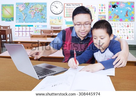 Portrait of young male teacher helps his student to study with laptop in the classroom