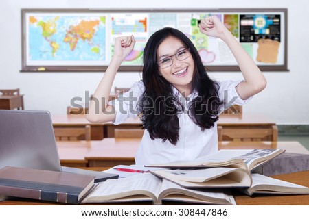 Portrait of beautiful female high school student with black hair, celebrating back to school and raise hands in the classroom