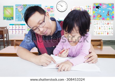 Portrait of male teacher guide a little girl to study and write on the book, shot in the classroom