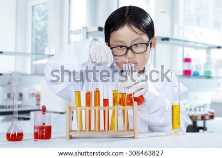 Portrait of schoolboy doing chemistry experiment while wearing coat in the laboratory
