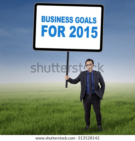 Asian businessman standing on the meadow while holding a board with number 2015