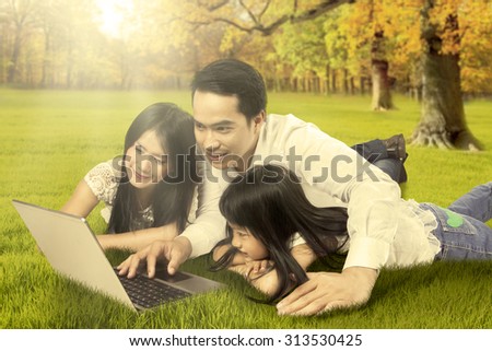 Image of happy asian family lying on the field while using laptop computer at the autumn park