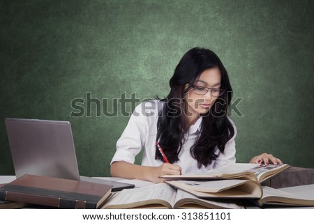 Female learner with long hair, sitting in the classroom while reading and write on the book