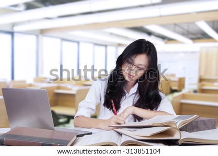 Image of a smart high school student sitting in the classroom while doing school assignment on the table