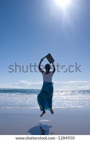 Woman carrying laptop computer jumping around at the beach