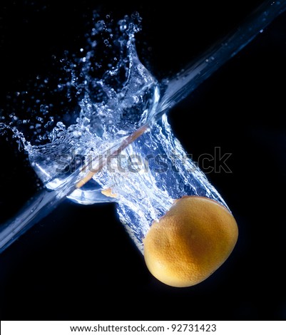 Fresh yellow orange splashing into water with water bubbles on black