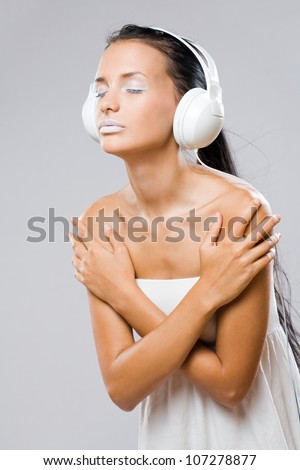 Portrait of a young tanned brunette in white makeup listening to music in white headphones.