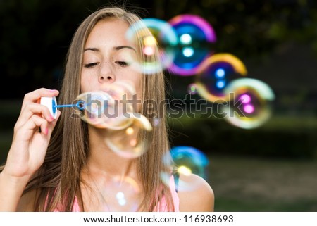 Dreamy blond teen beauty blowing soap bubbles.