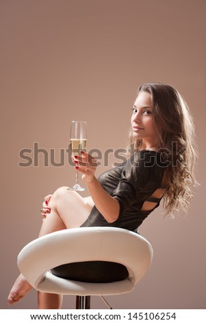 Portrait of festive brunette beauty on bar stool with glass of champagne.