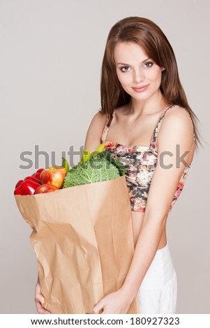 Gorgeous fit slender young brunette woman with bag of fresh vegetables.
