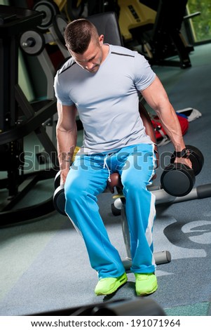 Portrait of a handsome young man doing arm exercises in a gym.