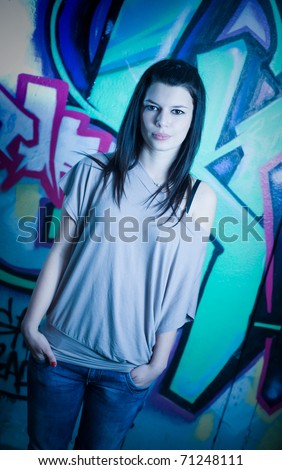 Urban portrait of a beautiful young brunette girl with graffiti background, serious facial expression