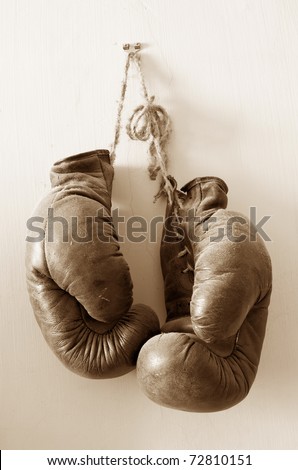 hang up the gloves, old worn leather boxing gloves in sepia tones, hanged up on grunge style wall.