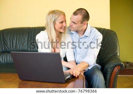 Cute young couple using laptop at home sitting on leather couch.