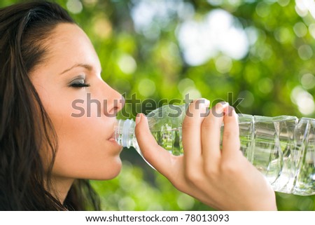 Beautiful young brunette in sunshine, drinking water from a bottle.