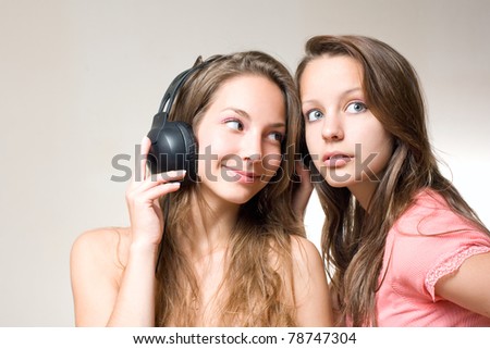 Two beautiful young brunettes sharing their music playing with their headphones.