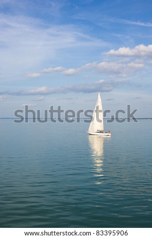 Sailing away on blue waters with strip of land behind.