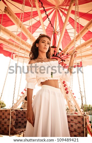 young woman in white summer dress in amusement park stand by carousel