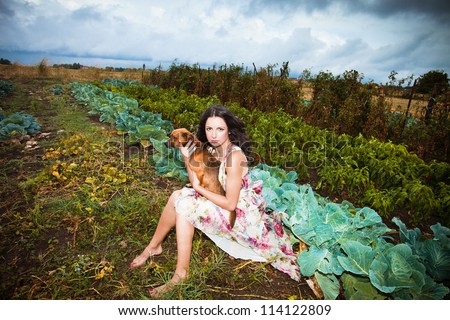 beautiful girl in elegant floral dress barefoot sit in autumn vegetable garden  at village holding a small dog