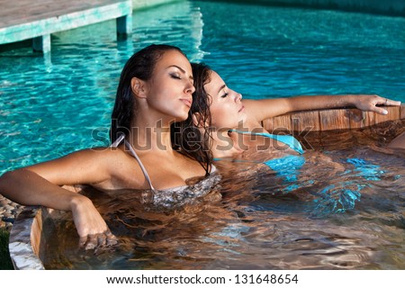 young women relaxing in outdoor jacuzzi by the pool summer day