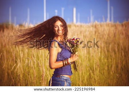 smiling beautiful woman with long curly hair in motion  hold in hand a bouquet of wild flowers in  grass field